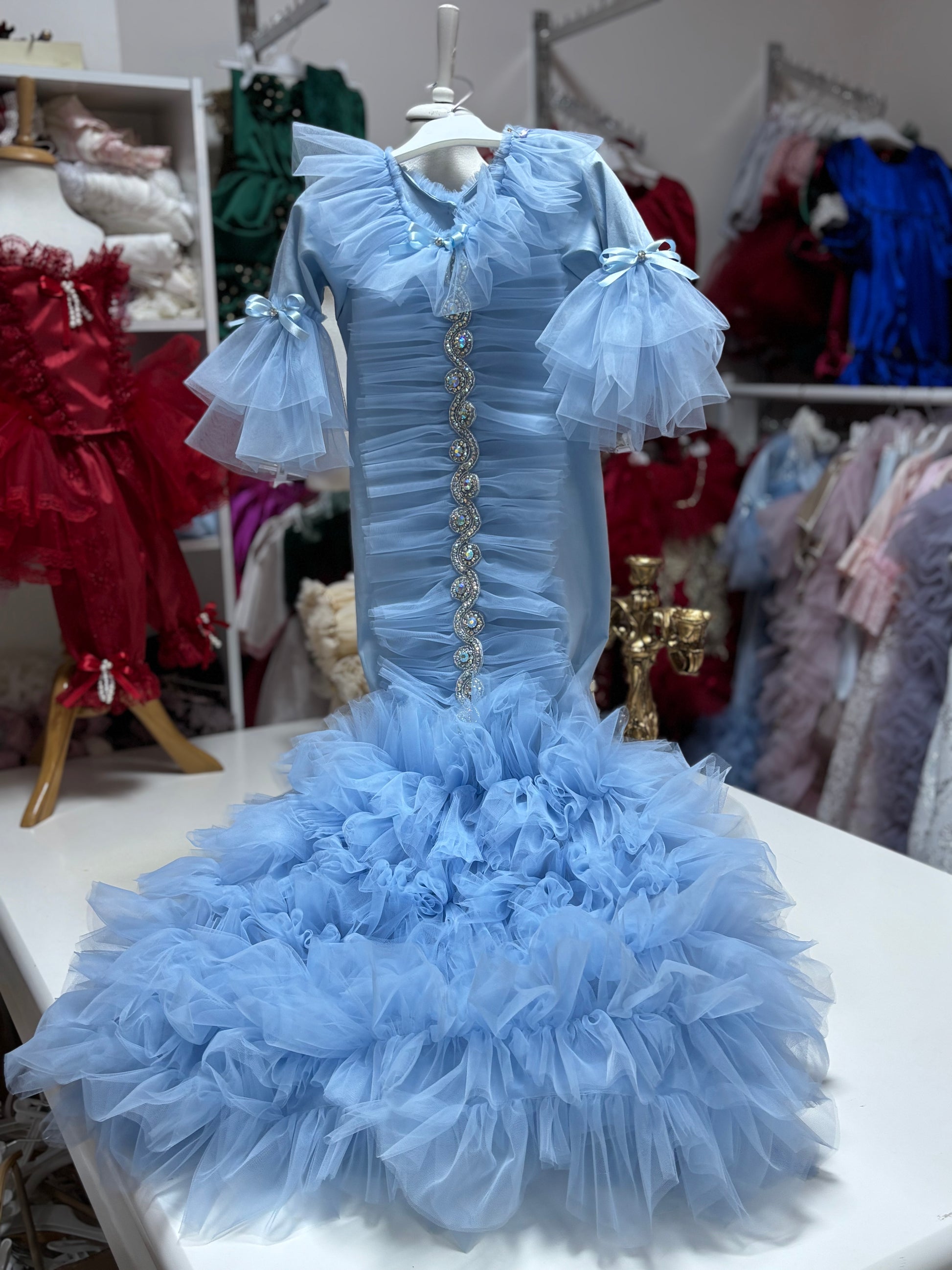 Light blue ruffled dress on a mannequin with a blurred background of other dresses.