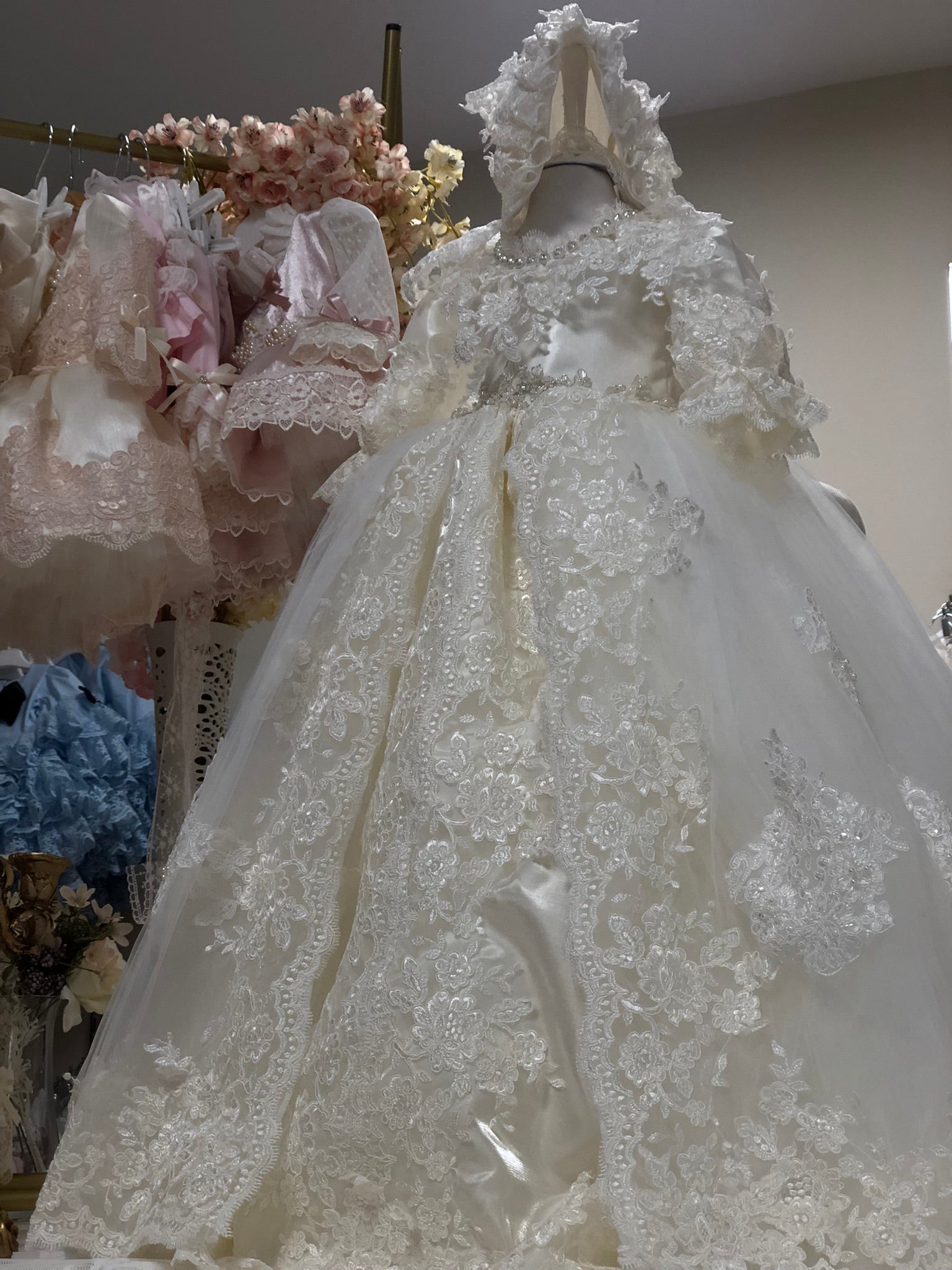 Elegant white lace wedding dress on a mannequin with floral decorations in the background.