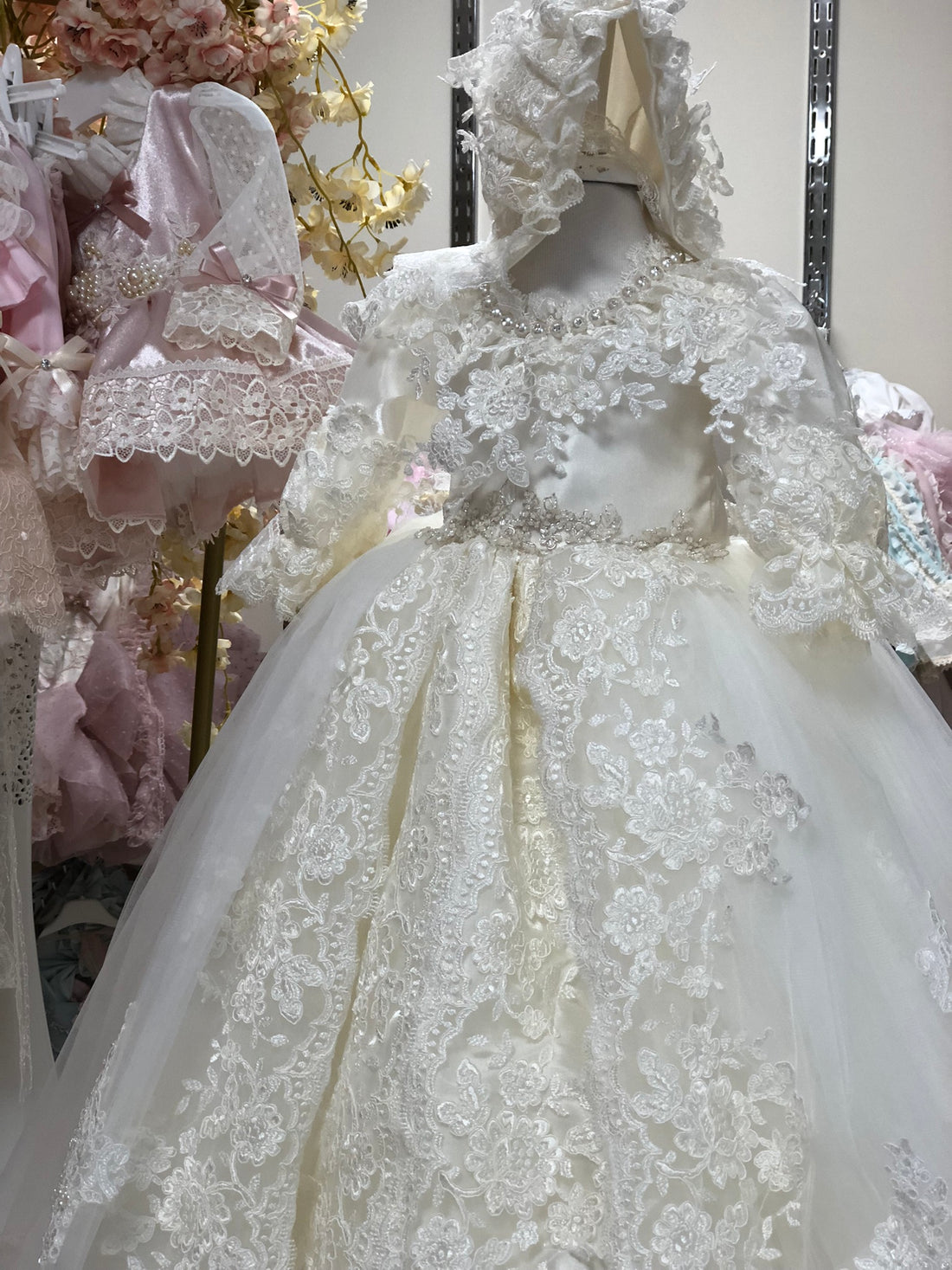 Elegant white lace wedding dress on a mannequin with floral decorations in the background.